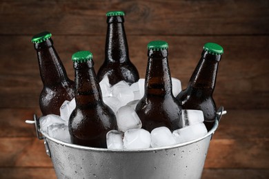 Metal bucket with bottles of beer and ice cubes on wooden background, closeup