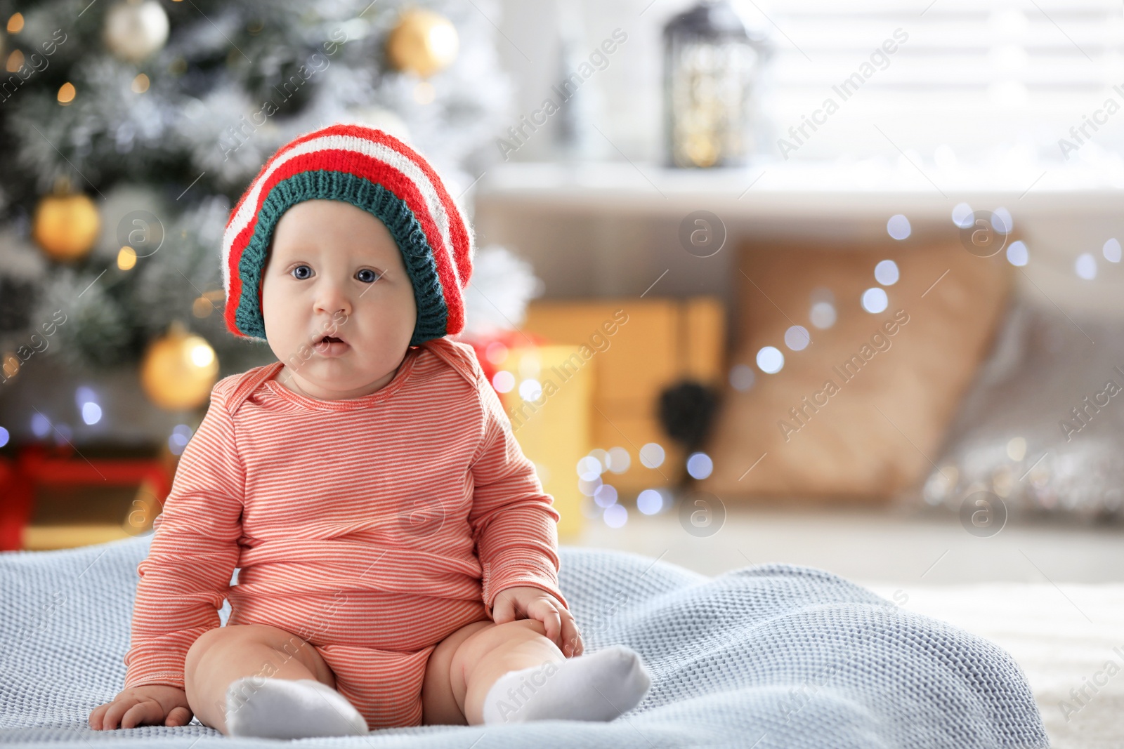 Photo of Little baby wearing elf hat on blanket indoors. First Christmas