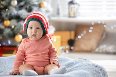 Little baby wearing elf hat on blanket indoors. First Christmas