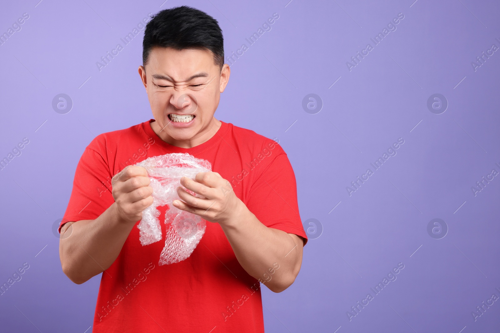 Photo of Emotional asian man with bubble wrap on purple background. Space for text