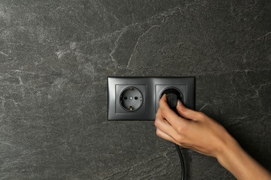 Photo of Woman putting plug into socket indoors, closeup