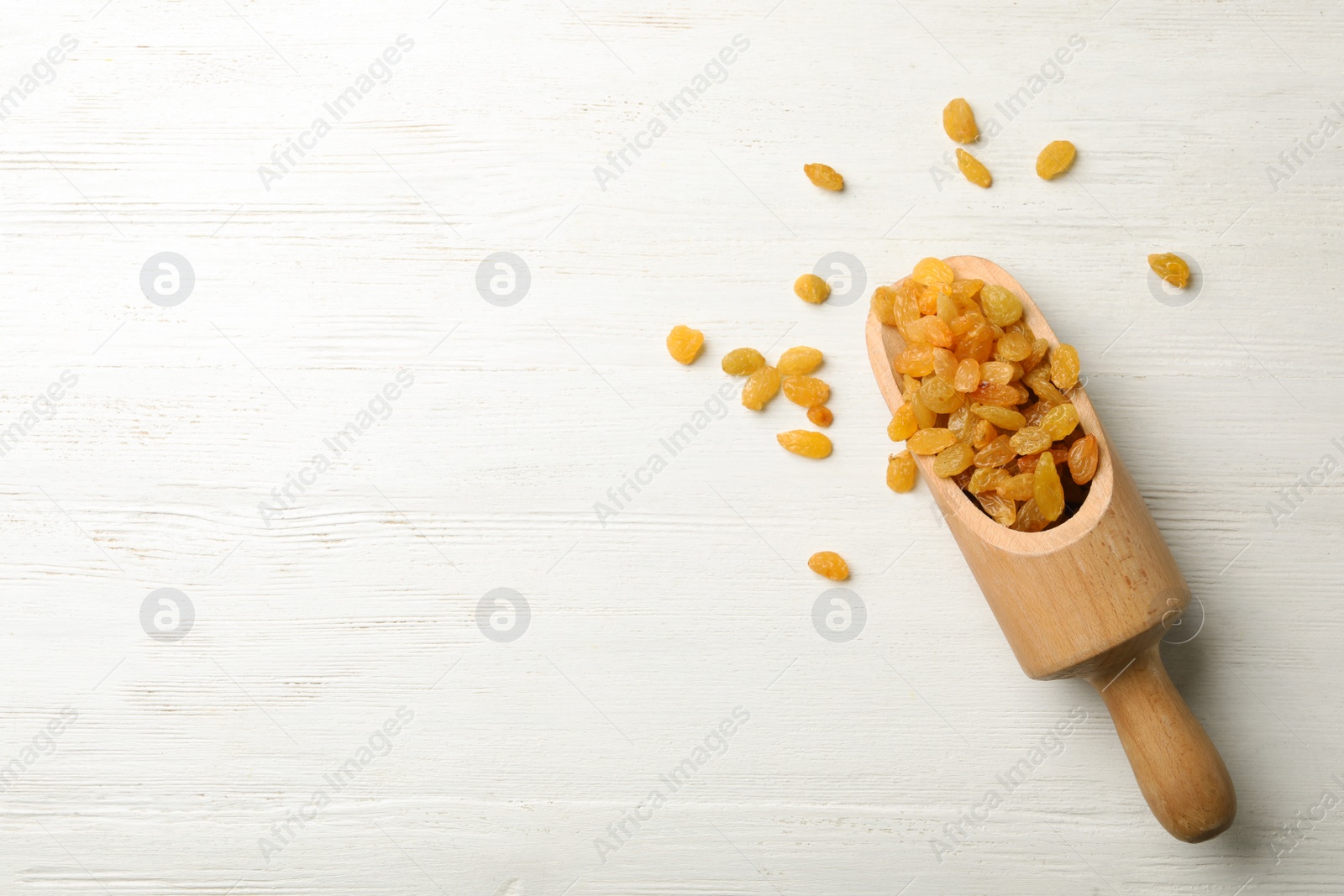 Photo of Scoop of raisins on wooden background, top view with space for text. Dried fruit as healthy snack