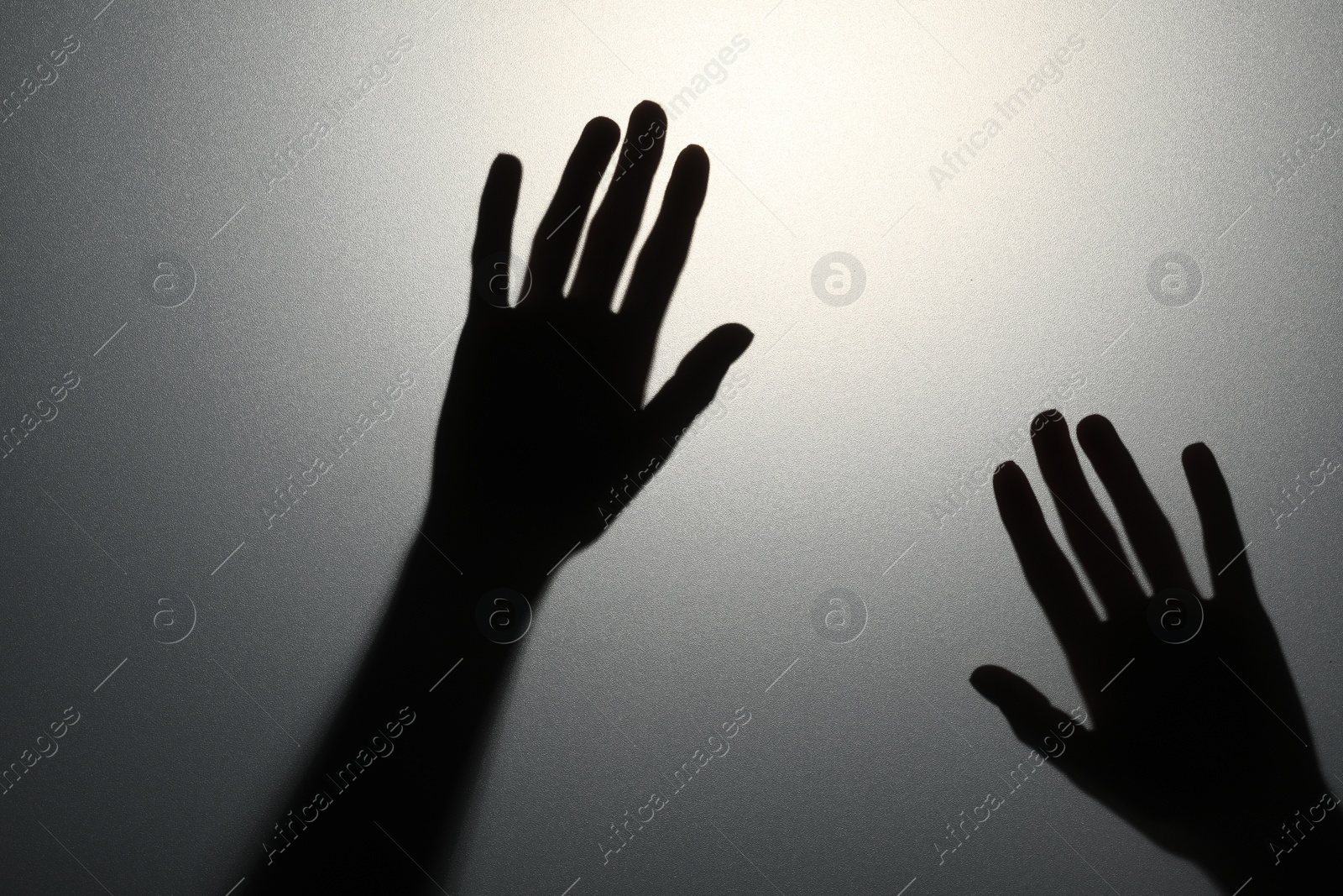 Photo of Silhouette of creepy ghost behind glass against grey background, closeup