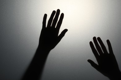 Photo of Silhouette of creepy ghost behind glass against grey background, closeup