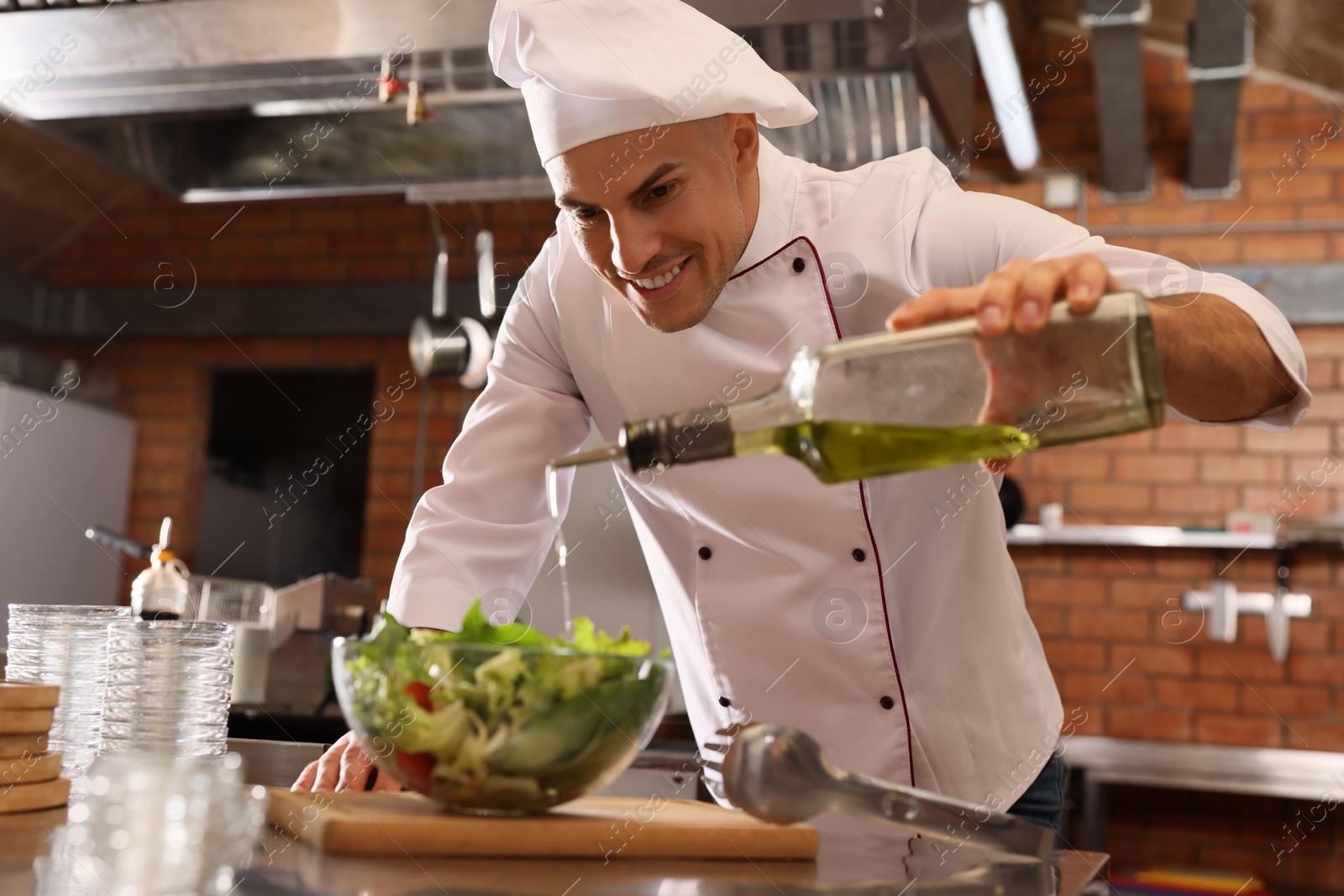 Photo of Professional chef pouring oil into bowl with fresh salad in restaurant kitchen