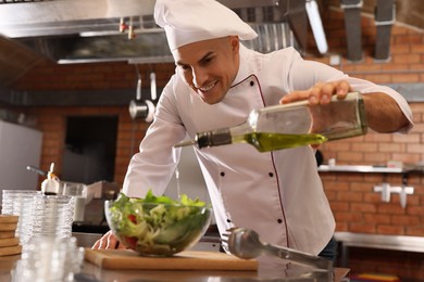 Professional chef pouring oil into bowl with fresh salad in restaurant kitchen