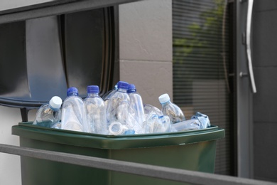 Many used plastic bottles in trash bin near entrance outdoors. Recycling problem