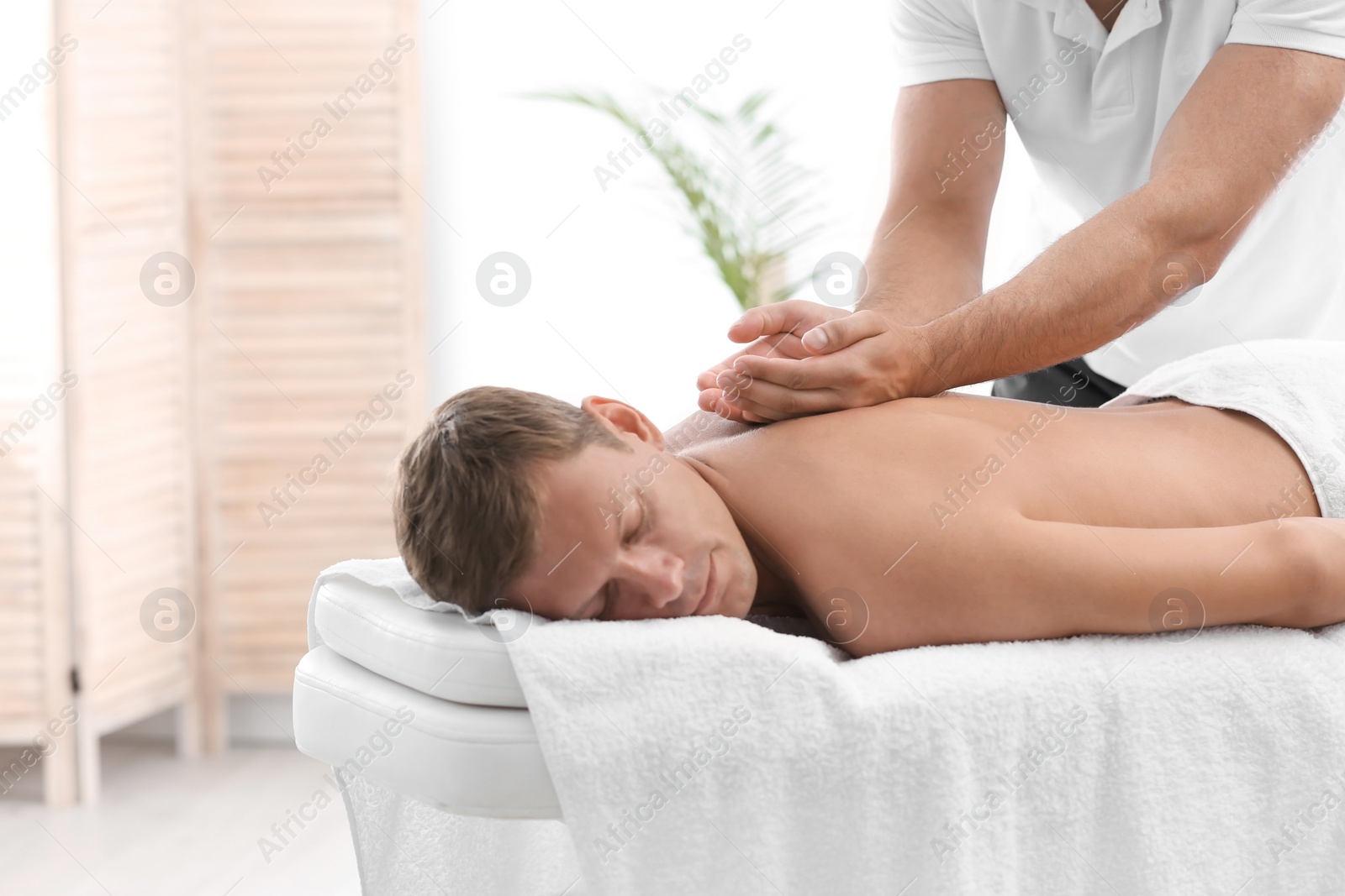 Photo of Relaxed man receiving back massage in wellness center