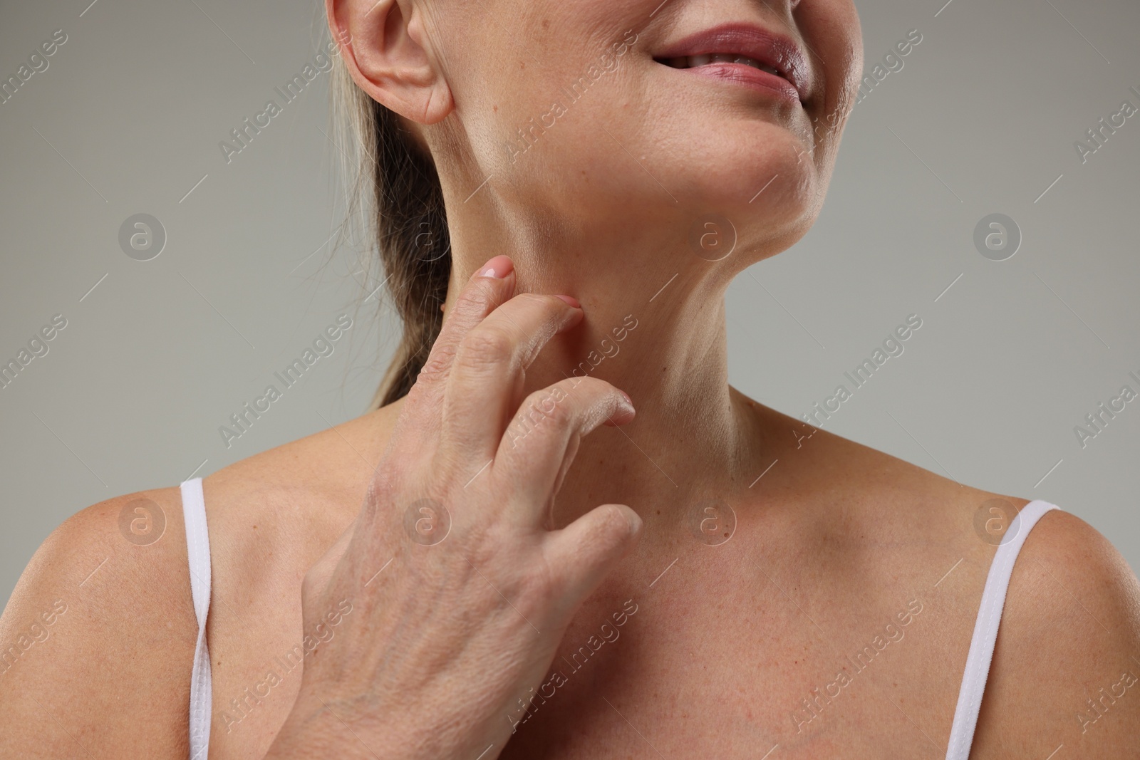 Photo of Mature woman touching her neck on grey background, closeup