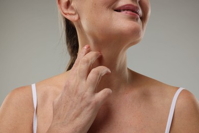 Photo of Mature woman touching her neck on grey background, closeup