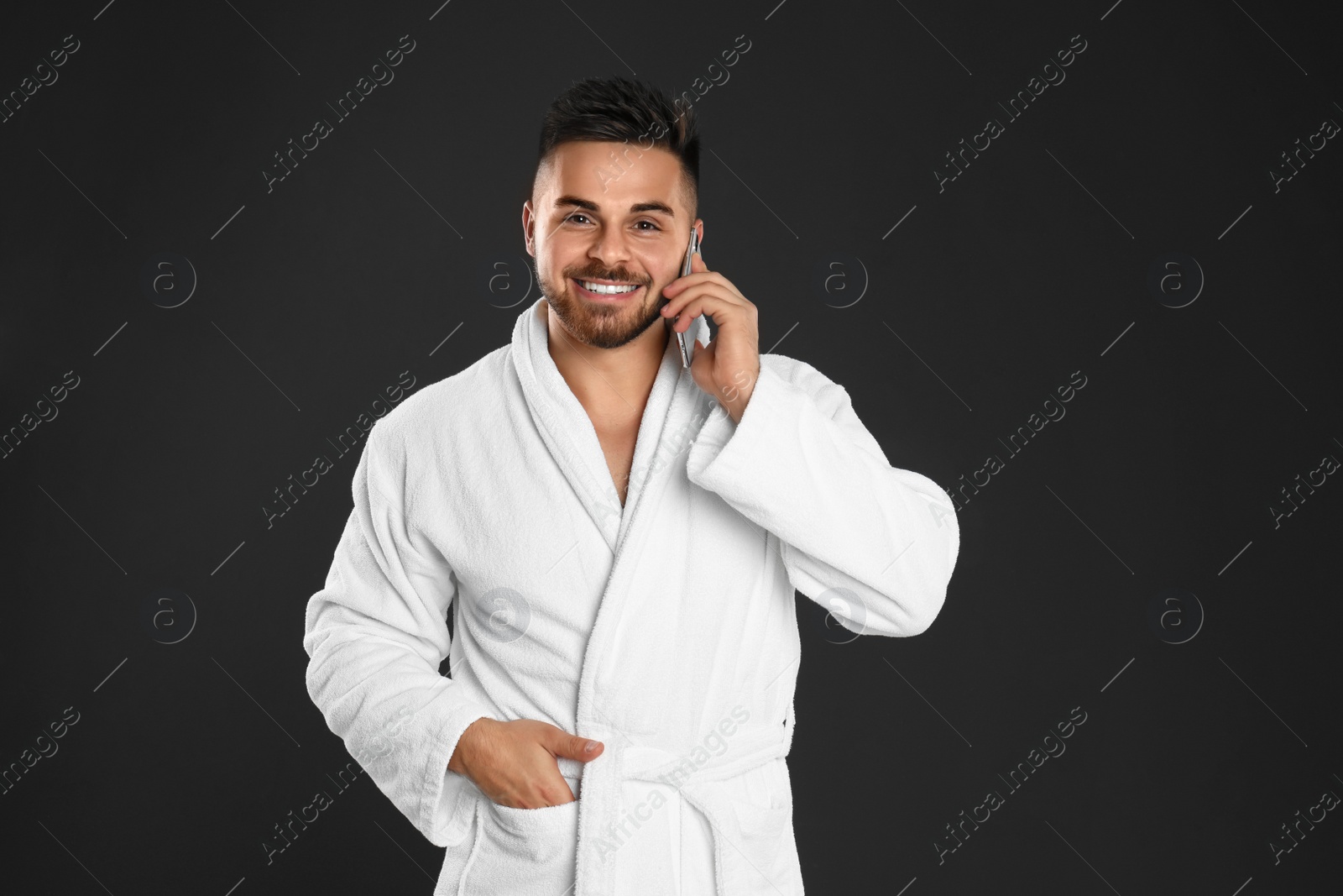 Photo of Young man in bathrobe talking on mobile phone against black background