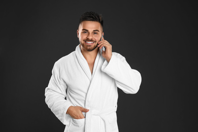 Photo of Young man in bathrobe talking on mobile phone against black background