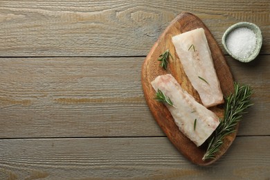 Photo of Fresh raw cod fillets, salt and rosemary on wooden table, flat lay. Space for text
