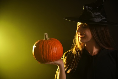 Photo of Young woman wearing witch costume with pumpkin on dark background. Halloween party