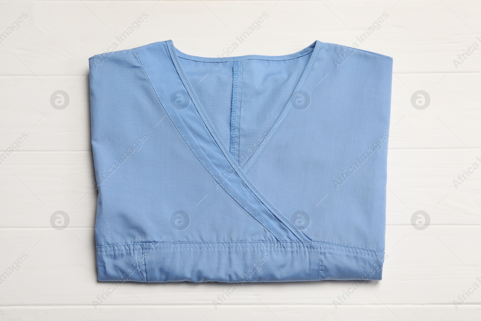 Photo of Light blue medical uniform on white wooden table, top view