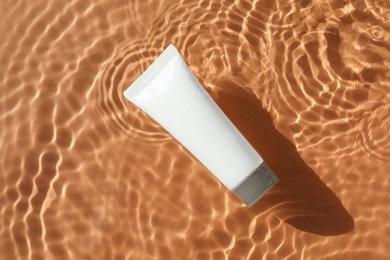 Photo of Tube with moisturizing cream in water on orange background, top view