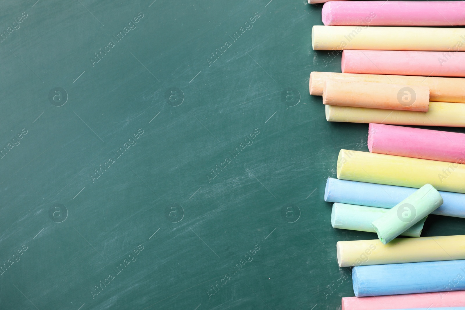 Photo of Pieces of color chalk on greenboard, flat lay. Space for text