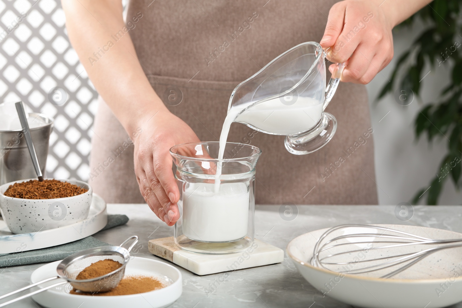 Photo of Making dalgona coffee. Woman pouring milk into glass at light gray table, closeup