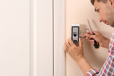 Photo of Young man installing fingerprint security alarm system indoors, closeup