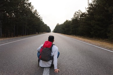 Photo of Man with backpack sitting on road near forest, back view