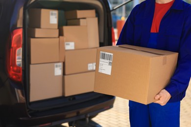 Photo of Courier with parcel near delivery van outdoors, closeup. Space for text