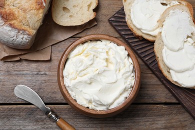 Photo of Fresh bread with delicious cream cheese on wooden table, flat lay