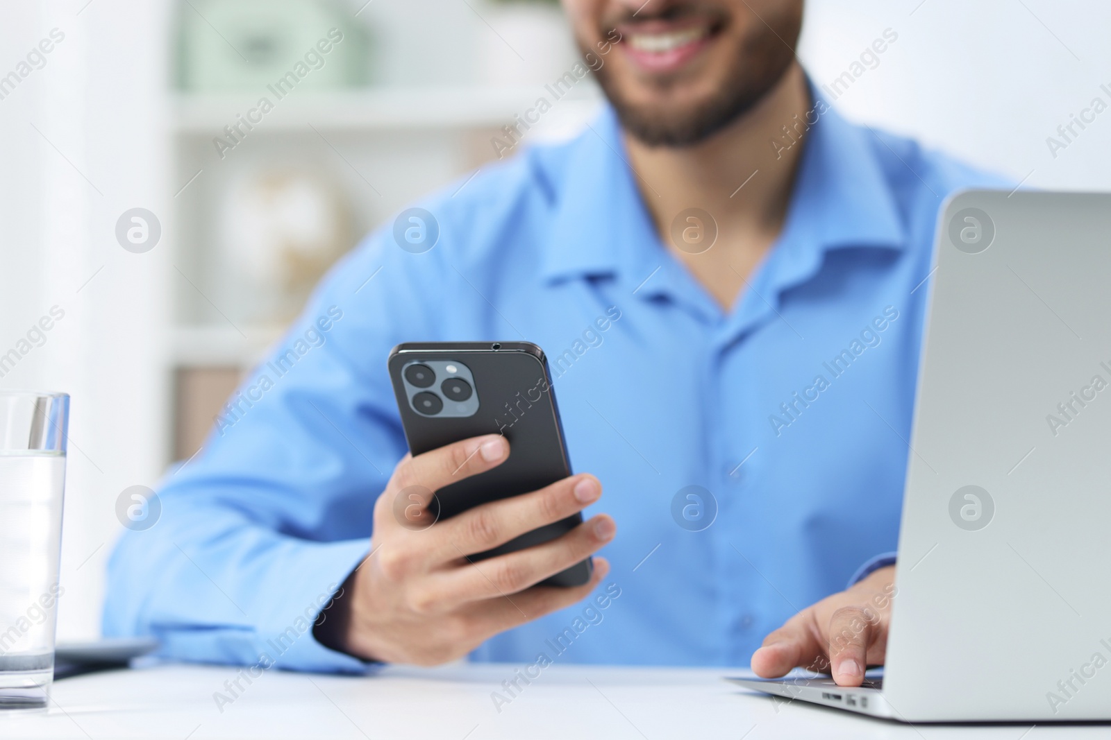 Photo of Man using smartphone while working with laptop at white table in office, closeup