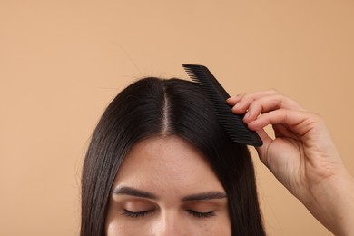 Photo of Woman with comb examining her hair and scalp on beige background, closeup