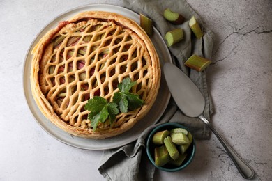 Photo of Freshly baked rhubarb pie, cut stalks and cake server on light grey table, flat lay