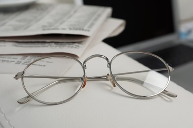Photo of Glasses and newspapers on armrest indoors, closeup