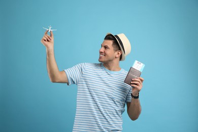 Photo of Male tourist holding passport with ticket and toy airplane on turquoise background