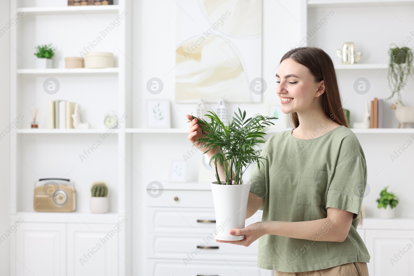 Photo of Beautiful young woman with green houseplant at home, space for text