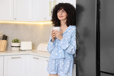 Photo of Beautiful young woman in stylish pyjama with cup of drink in kitchen