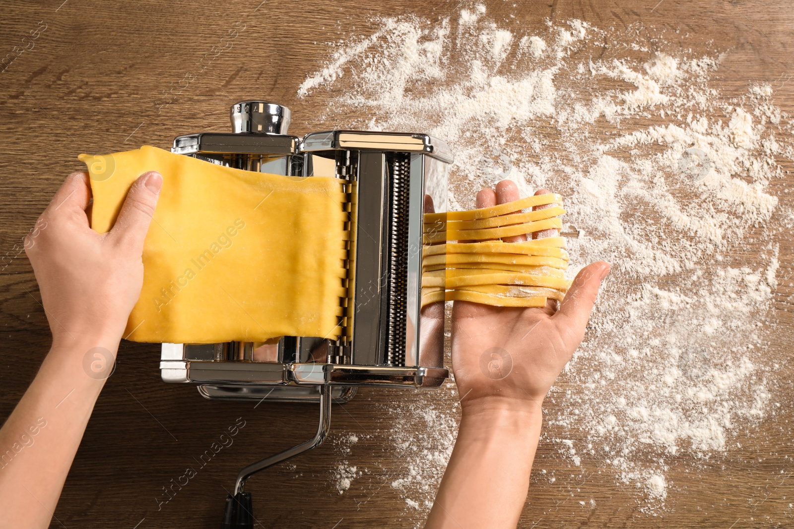 Photo of Woman preparing noodles with pasta maker machine at wooden table, top view