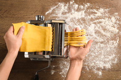 Woman preparing noodles with pasta maker machine at wooden table, top view