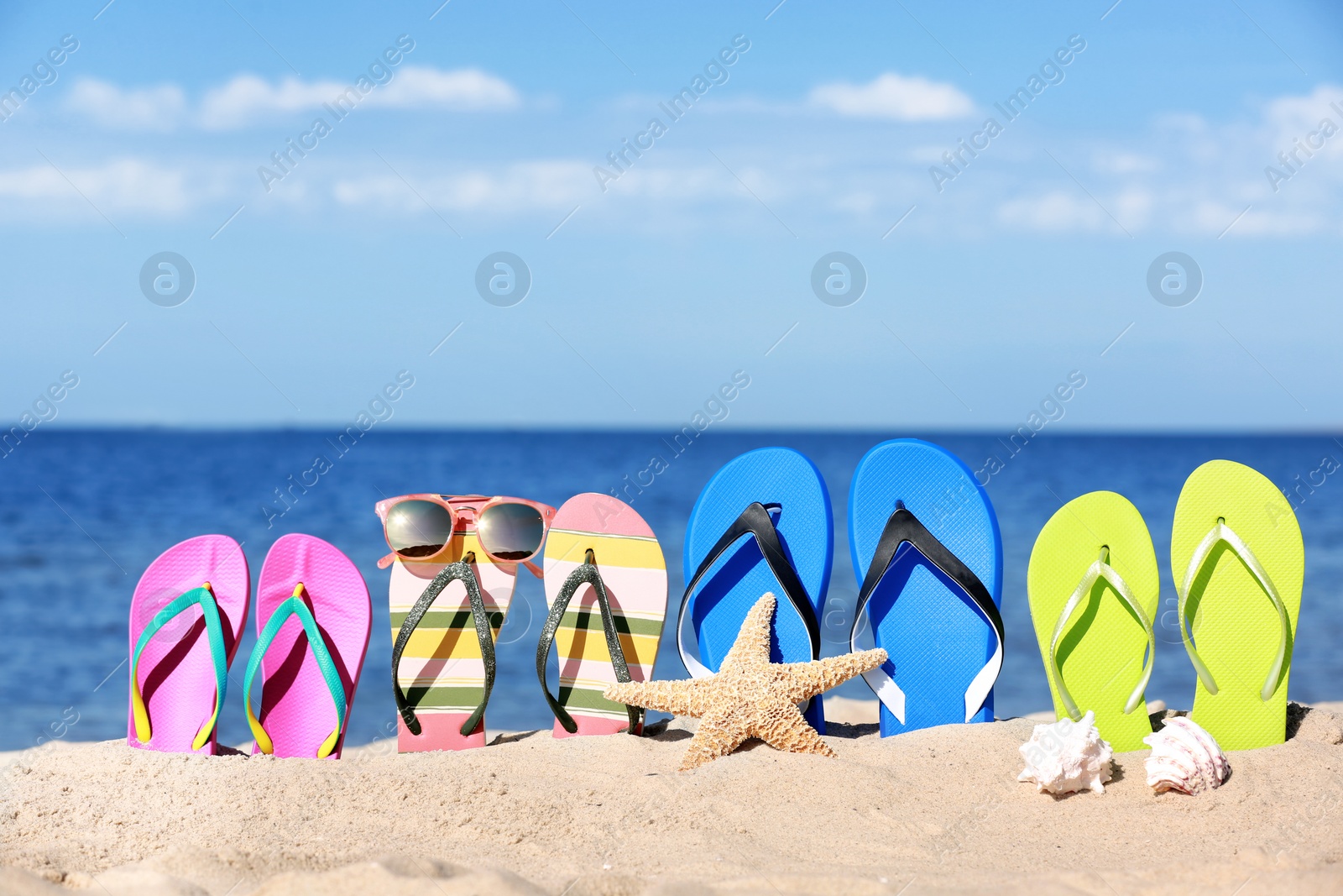 Photo of Composition with bright flip flops on sand near sea in summer. Beach accessories