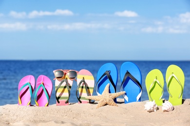 Composition with bright flip flops on sand near sea in summer. Beach accessories