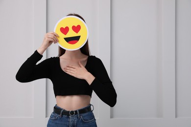 Woman covering face with heart eyes emoji near white wall, space for text