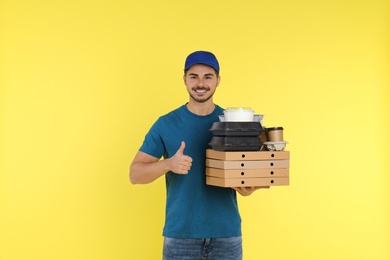 Young courier with different orders on color background. Food delivery service