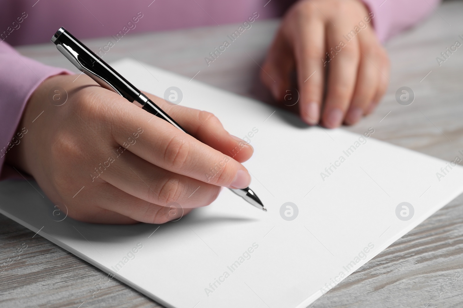 Photo of Woman writing on sheet of paper with pen at wooden table, closeup