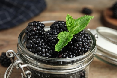 Glass jar of tasty blackberries and mint on table, closeup