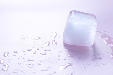 Photo of Crystal clear ice cube on light pink background, space for text