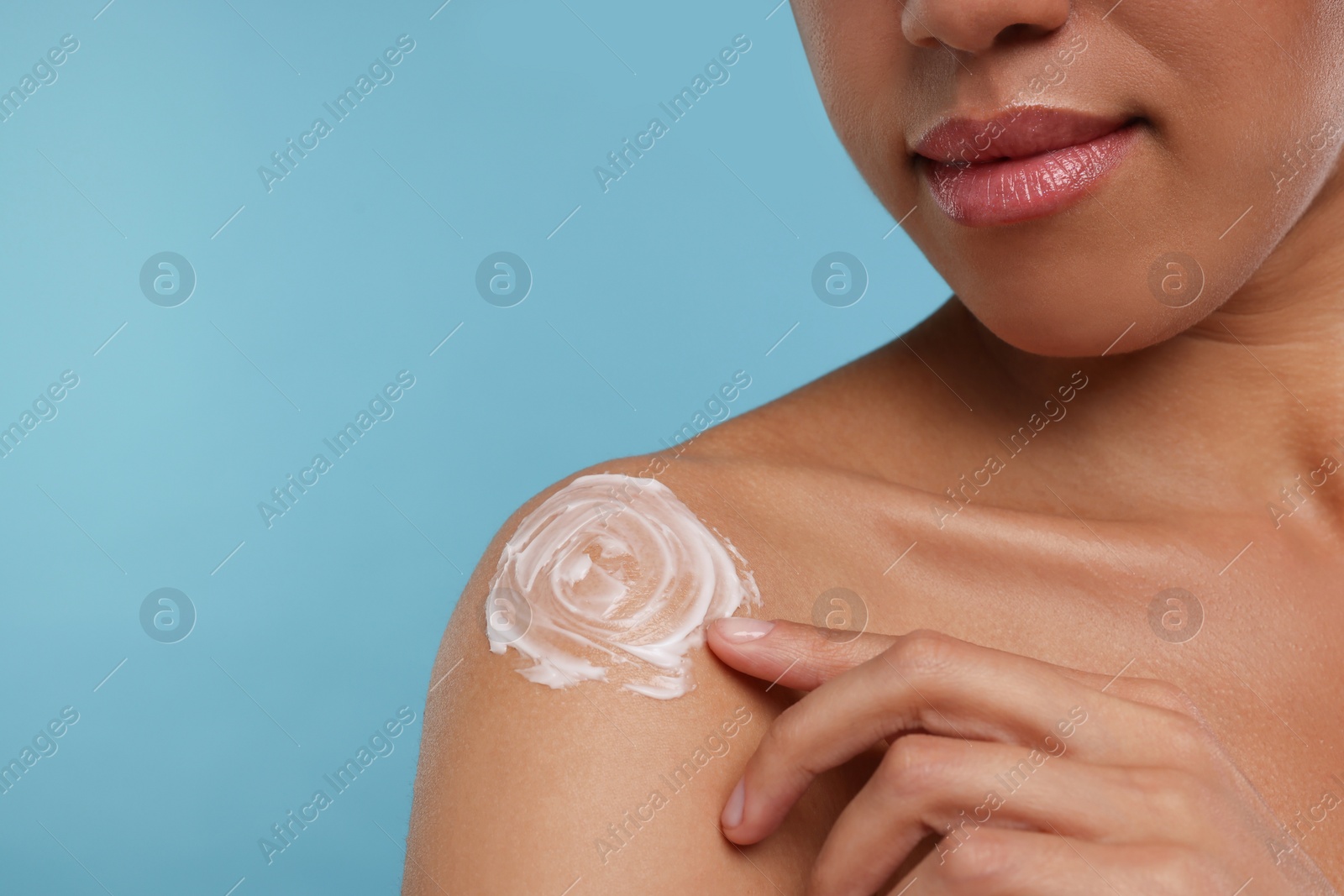 Photo of Young woman applying body cream onto shoulder on light blue background, closeup. Space for text