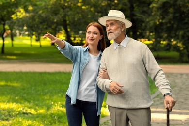 Senior man with walking cane and young woman in park