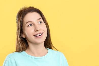 Photo of Portrait of smiling woman with dental braces on yellow background. Space for text