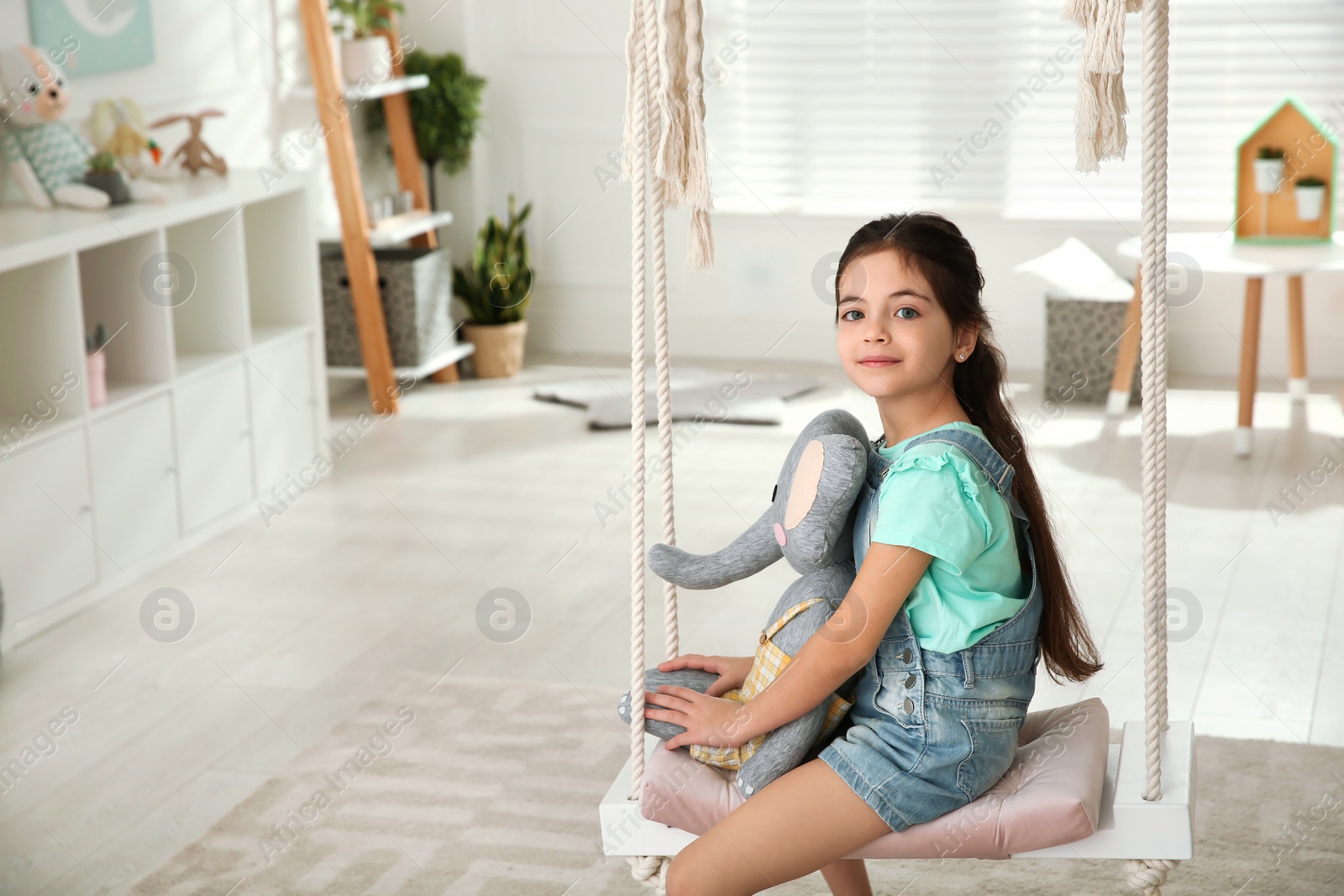 Photo of Cute little girl playing with toy elephant on swing at home. Space for text