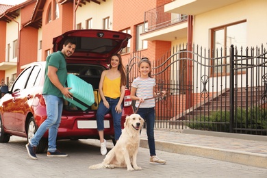 Photo of Happy family with dog and suitcase near car on street