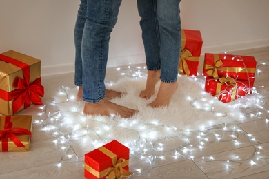 Photo of Young couple standing on rug near Christmas lights and gift boxes, closeup