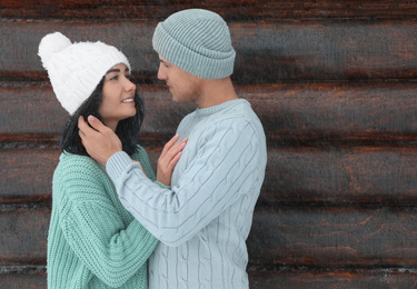 Lovely couple wearing warm sweaters and hats near wooden wall. Winter season