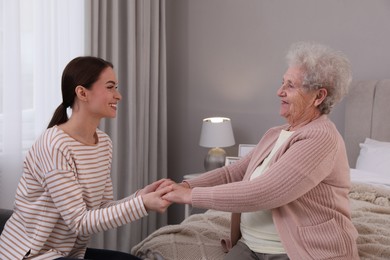 Photo of Young caregiver talking to senior woman in bedroom. Home health care service